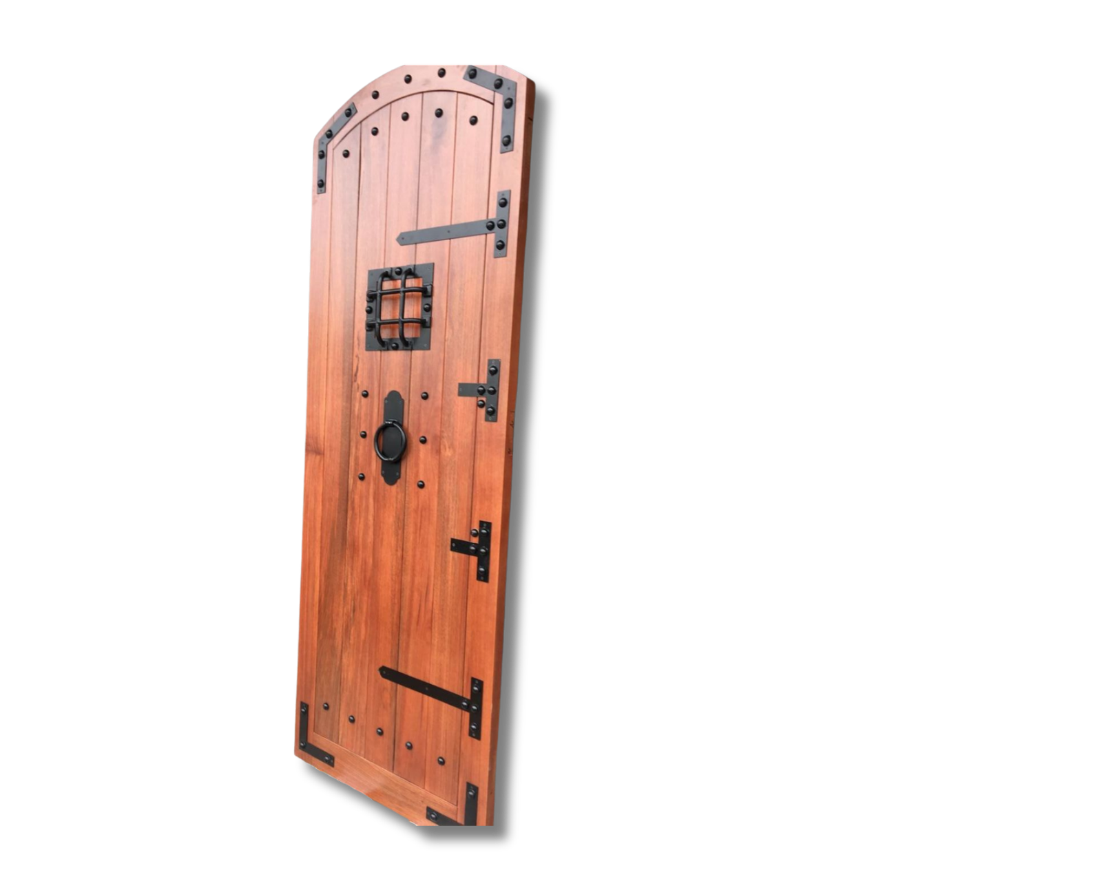 Arched rustic wooden door with black iron strap hinges, rivets, ring pull, and a small barred window grille on a black background