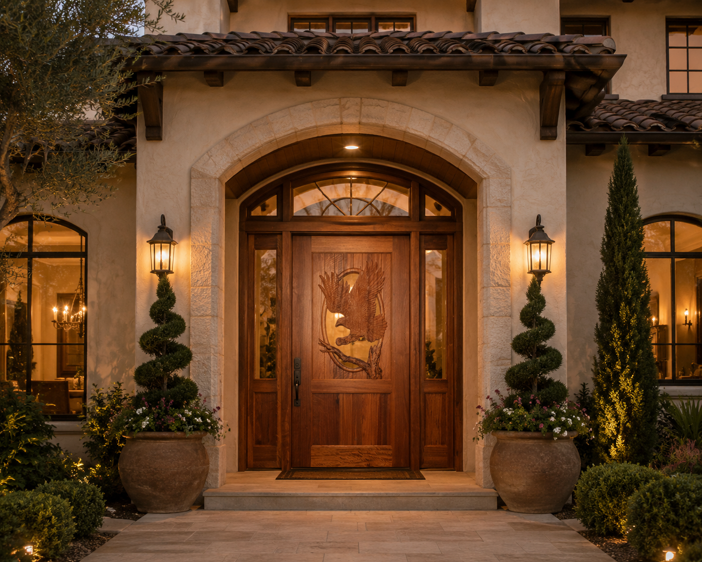 A grand villa entrance with a custom solid wood entry door featuring a large, hand-carved bald eagle design, framed by a stone archway, glass sidelights, and spiral topiaries