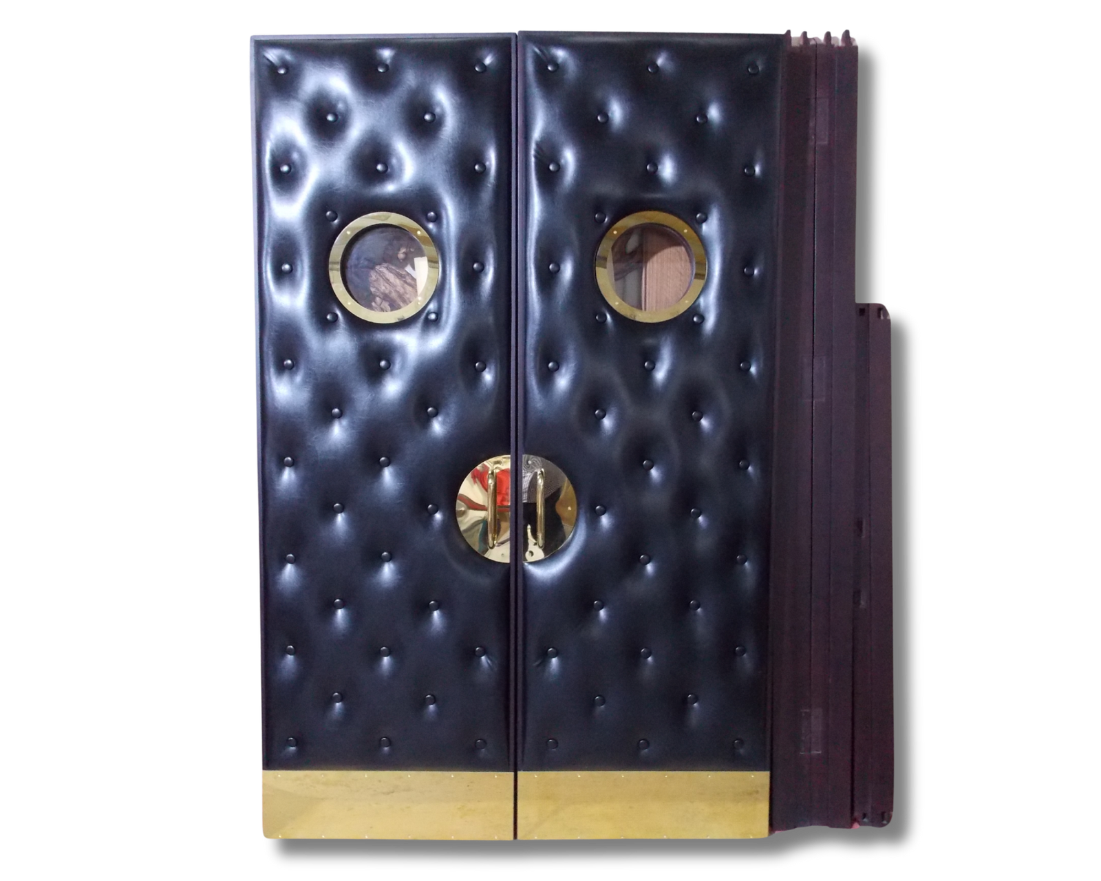 Custom upholstered double home theater doors by CROWNCUSTOMDOORS, featuring deep black tufted vinyl, circular brass vision panels, and matching polished brass hardware.