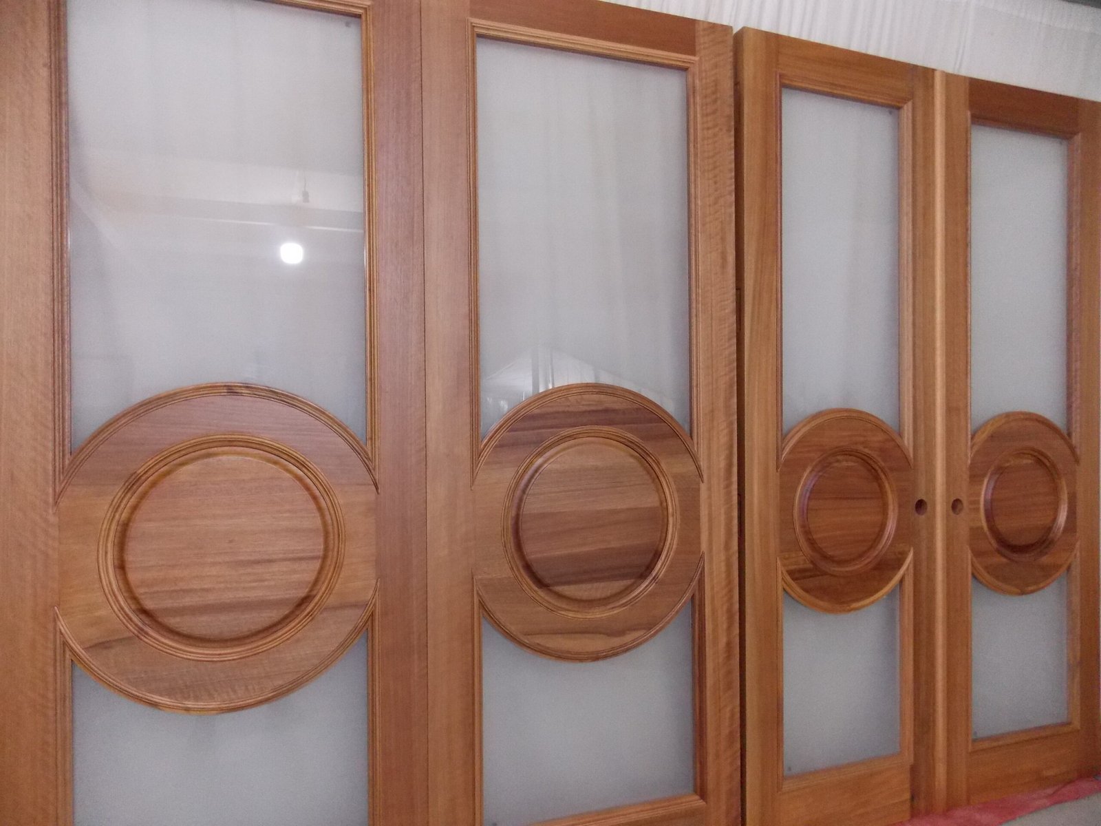 A detailed look at four custom handcrafted solid wood interior doors from the file crown-custom-doors-african-mahogany-frosted-glass-circular-panels.jpg, made of premium African Mahogany with frosted privacy glass inserts and a prominent central geometric circular medallion design.