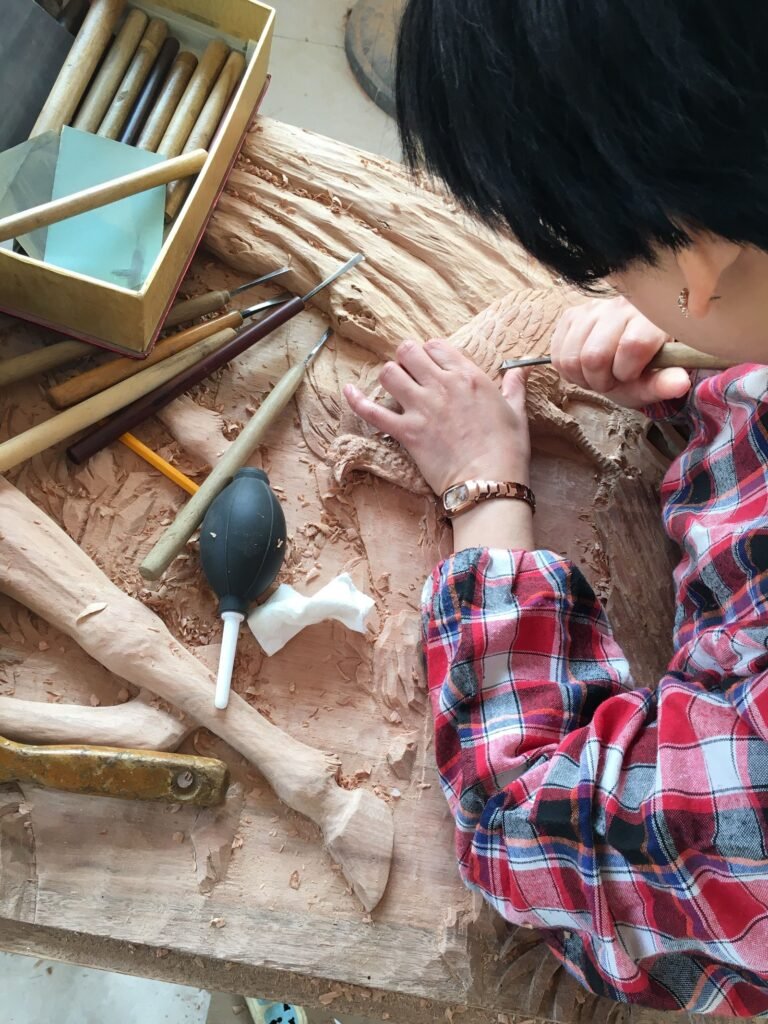 Overhead view of an artisan using fine hand chisels and traditional gouges to carve high-relief wildlife details on a solid wood door slab.
