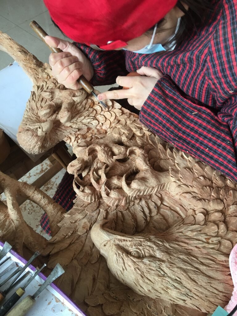 Master woodcarver using traditional chisel tools to hand-carve intricate eagle feathers in high-relief on a solid wood door panel.