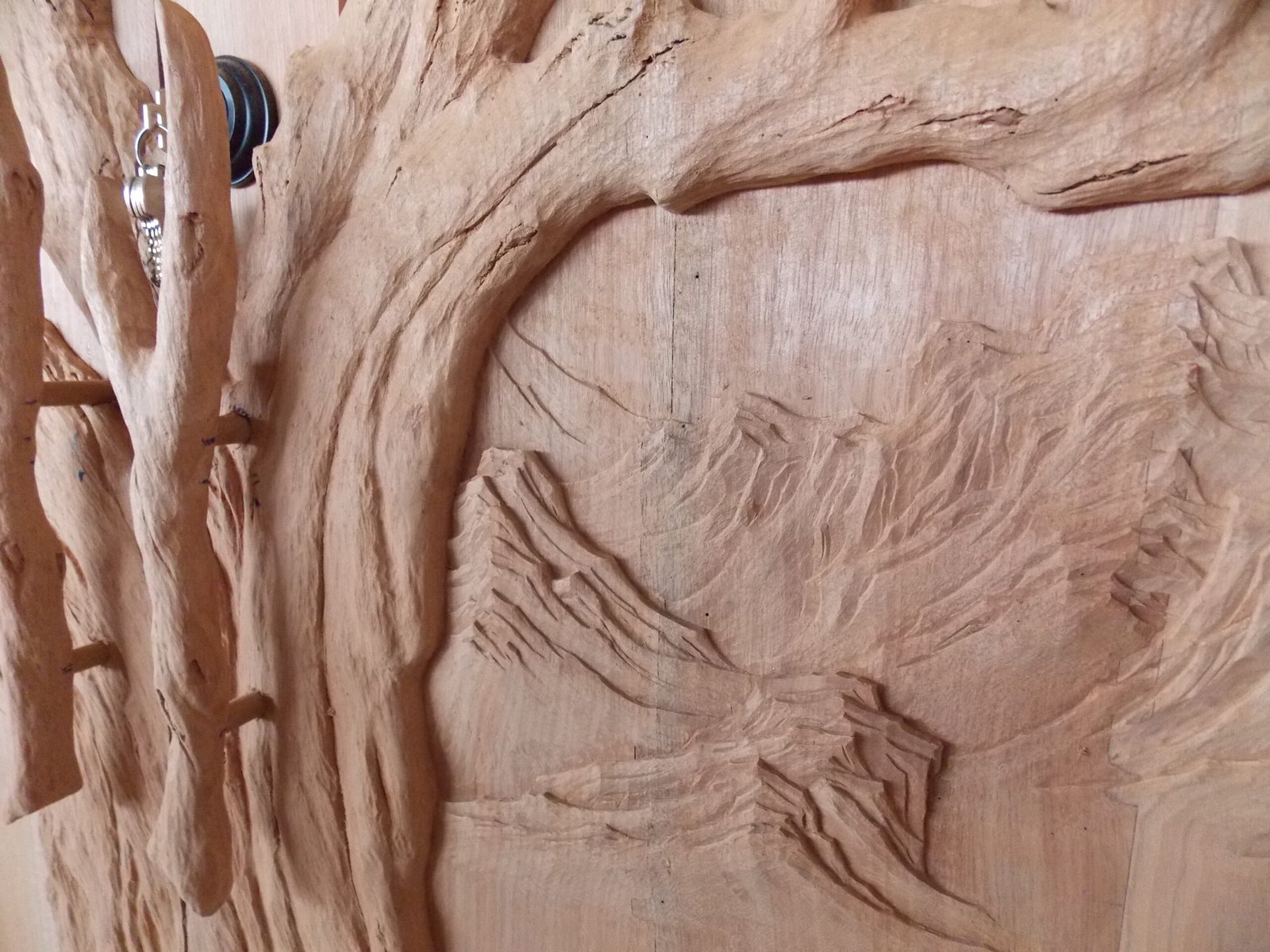 Extreme close-up of custom-carved branch door handles mounted on a solid wood Tree of Life entry door by Crown Custom Doors, highlighting high-relief bark textures and background mountain carvings.