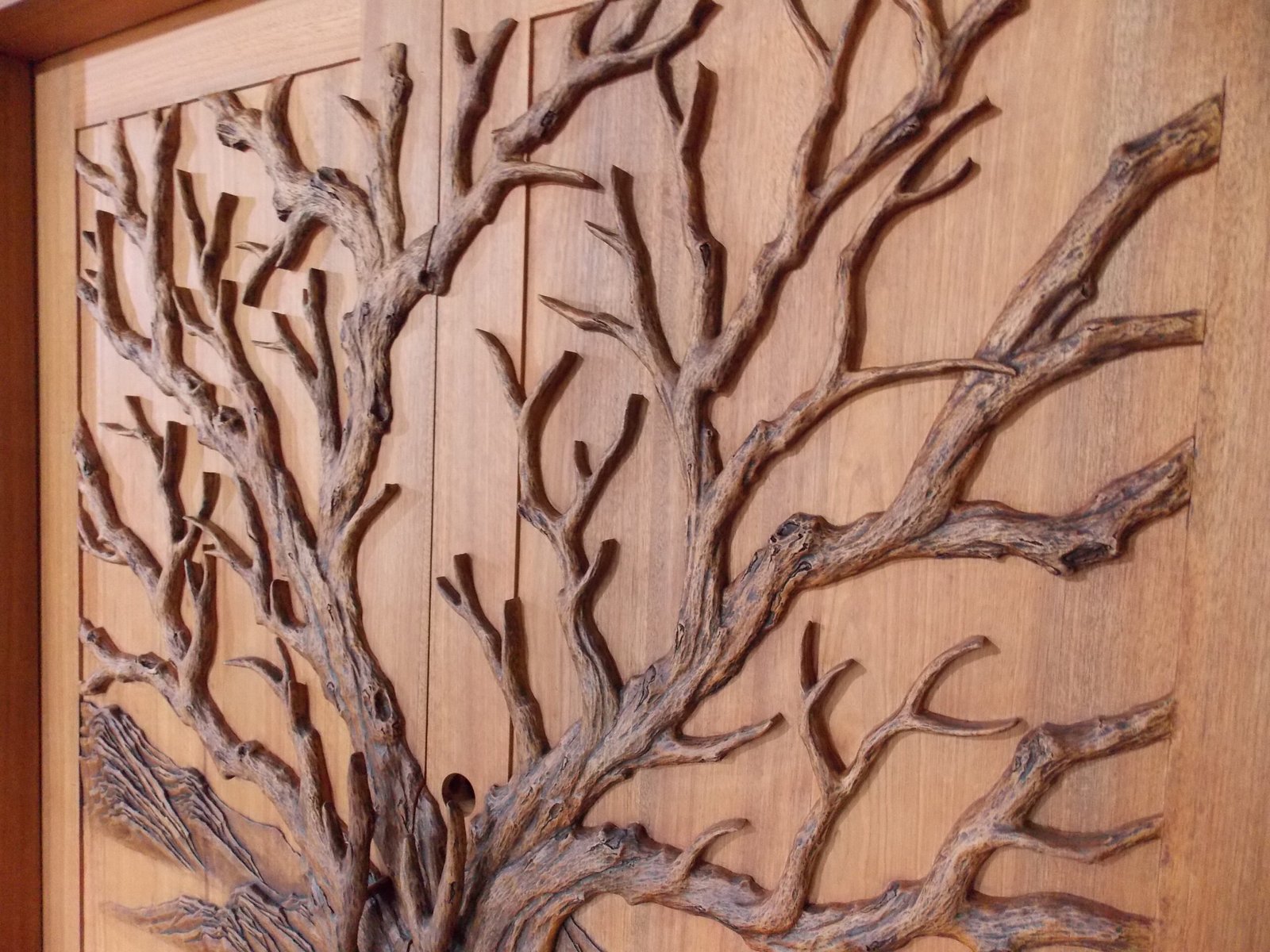 Angled close-up of the upper door section showing intricate hand-carved Tree of Life branches and canopy details on a stained solid wood double entry door by Crown Custom Doors.
