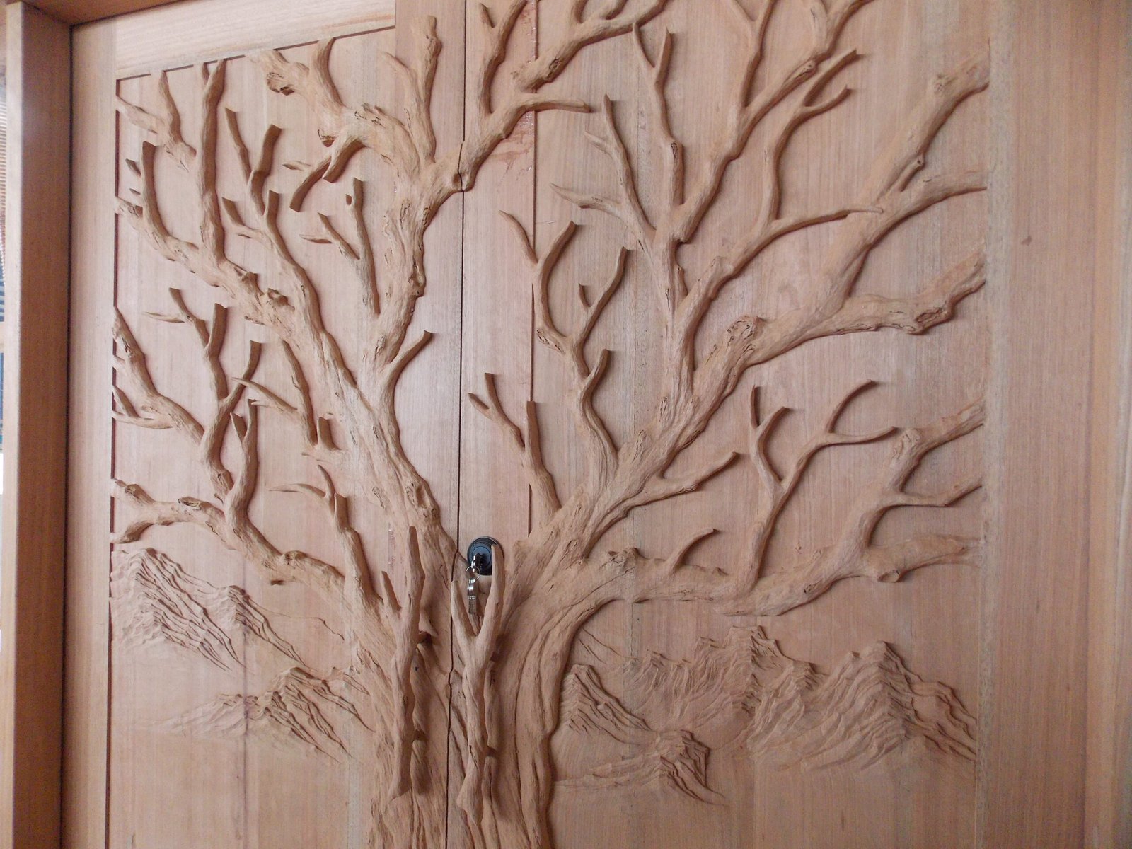 Assembled solid wood double entry door by Crown Custom Doors featuring a high-relief hand-carved Tree of Life motif, mountain backdrop, and custom branch door handles in a Craftsman door jamb.