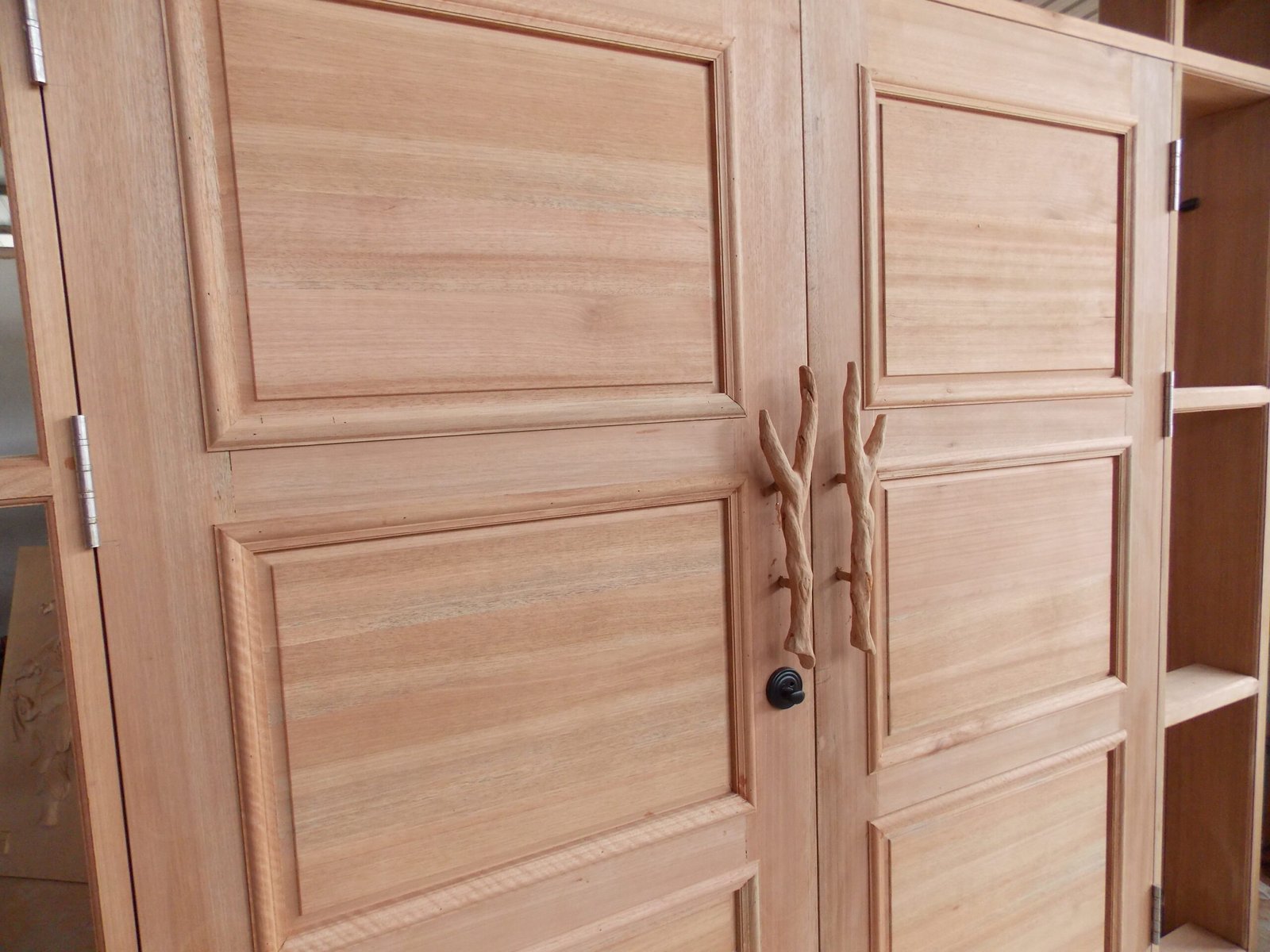 Close-up interior view of a solid wood double entry door by Crown Custom Doors showing classic raised panels, hand-sculpted branch handles, deadbolt lock hardware, and heavy-duty ball-bearing hinges.