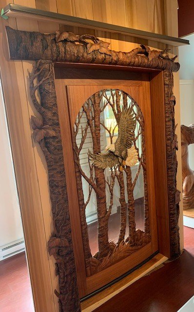 Interior perspective view of a custom hand-carved solid mahogany bald eagle front door featuring an arched glass relief panel, flat-top header, and matching sculpted tree bark casing for a yurt.