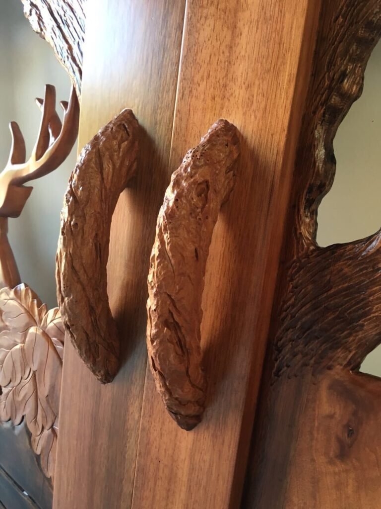 Close-up detail of custom hand-carved organic wood branch door handles mounted on a solid wood double entry door for a rustic craftsman home.
