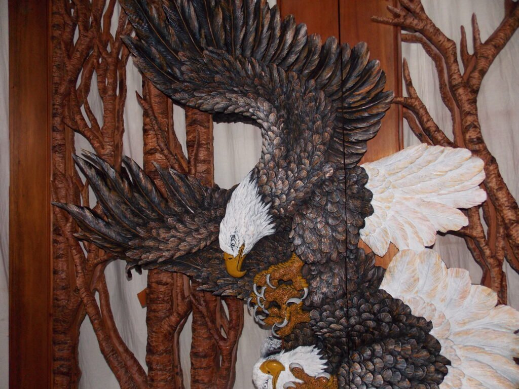Intricate hand-carved solid wood door panel depicting a soaring bald eagle in relief carving with detailed feathers and natural tree branch accents.