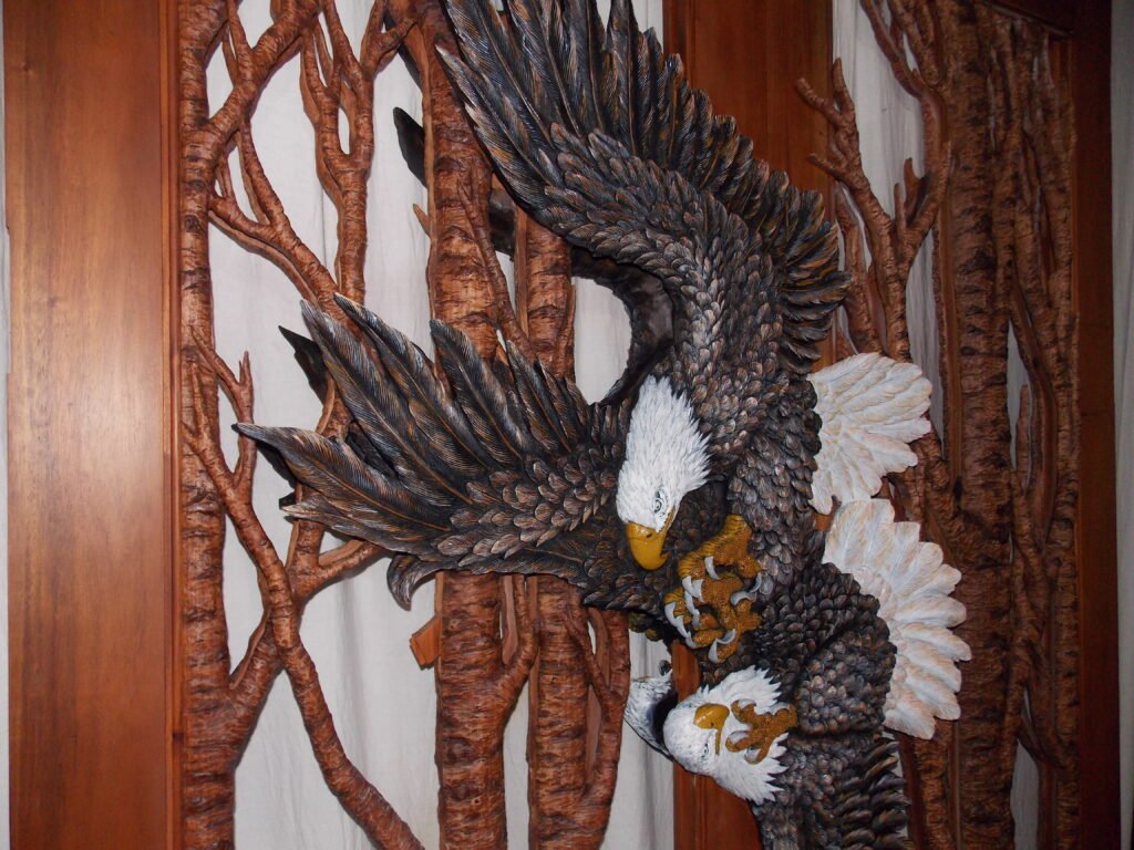 Vertical view of a completed solid wood door panel featuring two fully carved and painted bald eagles in flight with textured tree branch lattice accents.