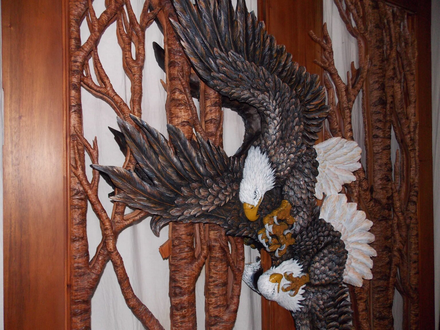 Vertical view of a completed solid wood door panel featuring two fully carved and painted bald eagles in flight with textured tree branch lattice accents.
