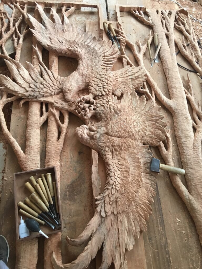 Finished raw hand-carved solid wood panel showing two eagles in flight surrounded by natural tree branch relief and traditional woodworking chisels.