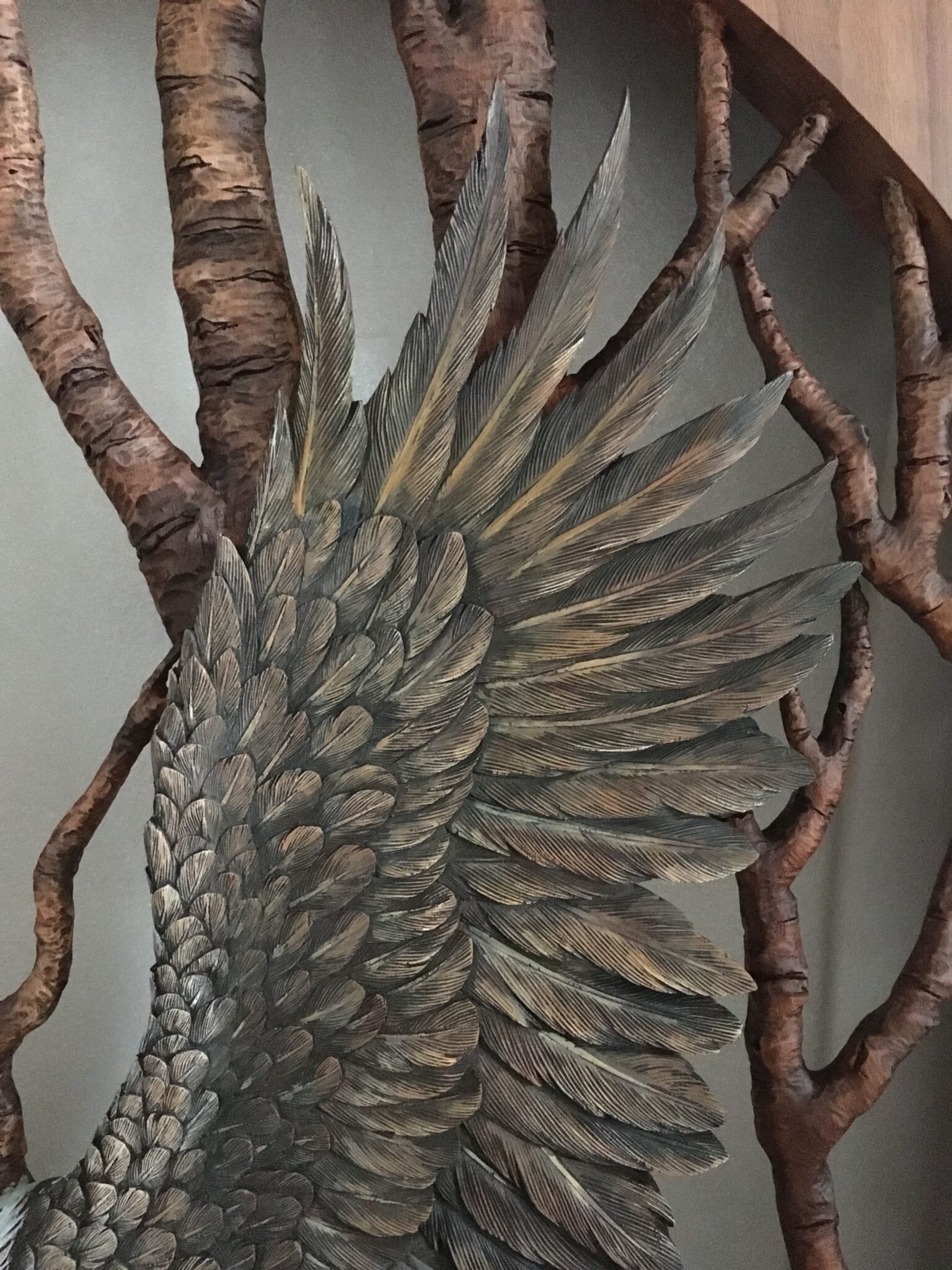 Extreme close-up shot of the hand-carved and painted raised wing feathers of a mahogany bald eagle against a backdrop of carved birch tree branches.