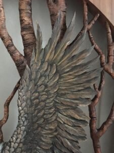 Extreme close-up shot of the hand-carved and painted raised wing feathers of a mahogany bald eagle against a backdrop of carved birch tree branches.
