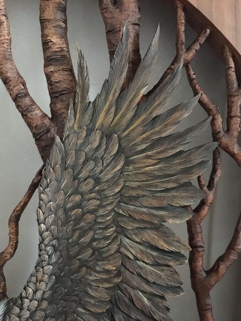 Extreme close-up shot of the hand-carved and painted raised wing feathers of a mahogany bald eagle against a backdrop of carved birch tree branches.