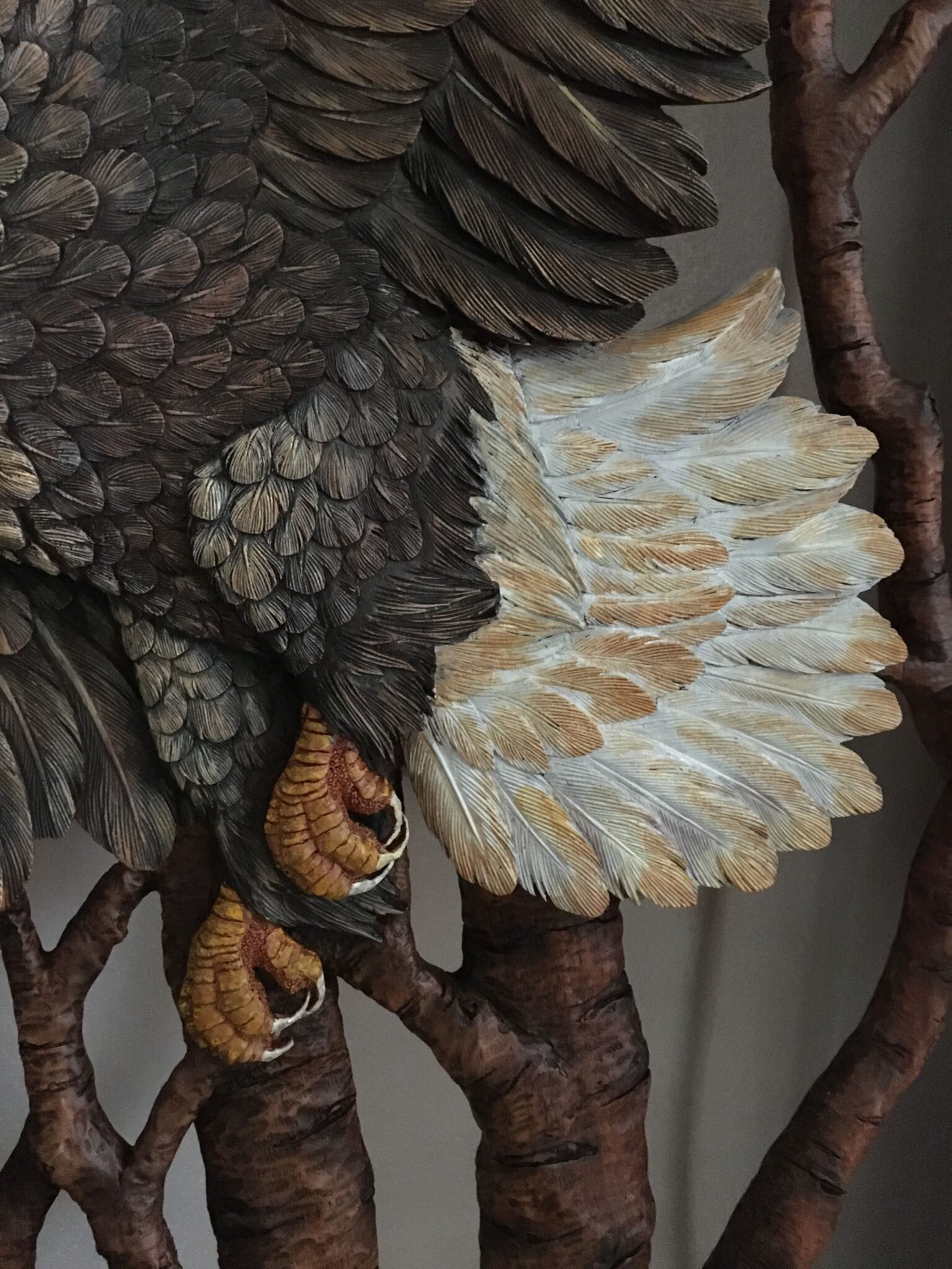 Extreme close-up shot of the hand-painted yellow talons, textured body feathers, and fan-shaped white tail feathers of a carved mahogany bald eagle on a custom front door.
