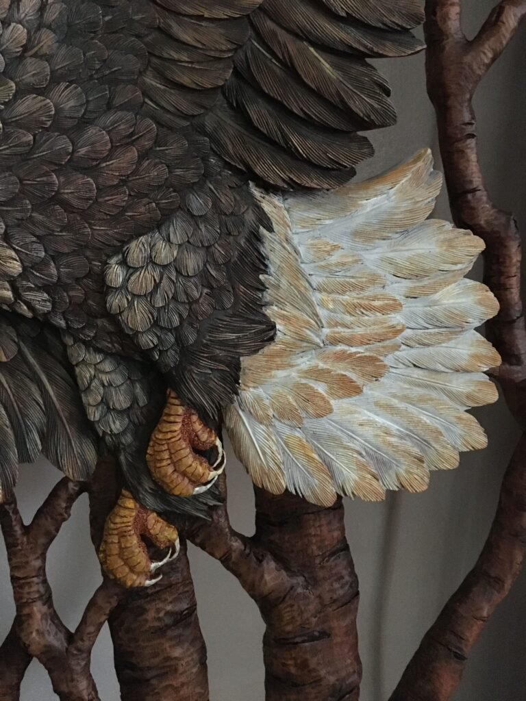 Extreme close-up shot of the hand-painted yellow talons, textured body feathers, and fan-shaped white tail feathers of a carved mahogany bald eagle on a custom front door.