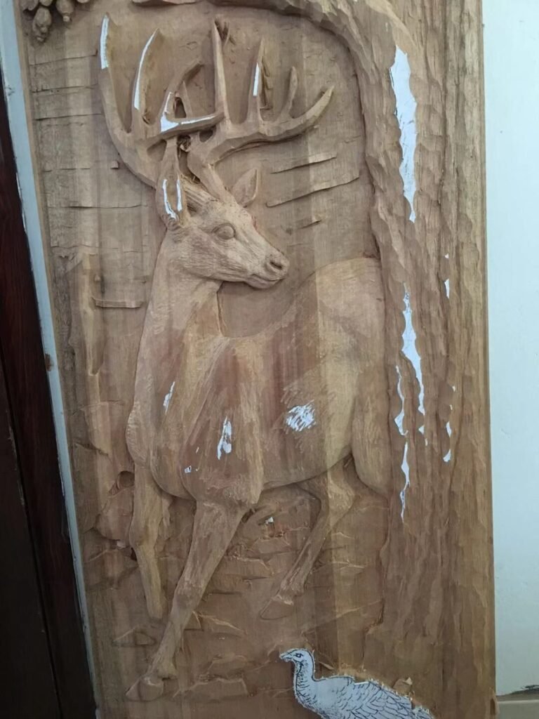 In-progress hand-carved solid wood door panel showing a trophy buck deer and wild turkey carved in deep relief before staining.