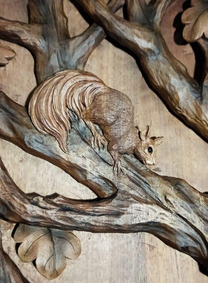 Close-up view of a hand-carved solid wood panel showing a detailed squirrel perching on oak tree branches with oak leaf accents.