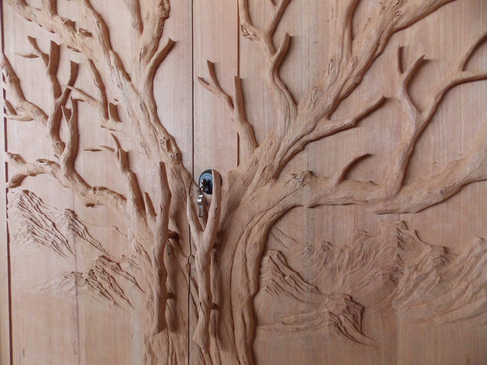 High-relief hand-carved Tree of Life design on solid wood double entry doors featuring custom branch door handles and mountain landscape details.