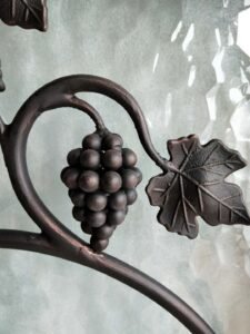 Extreme close-up of a detailed hand-forged wrought iron grape cluster and vine leaf with an oil-rubbed bronze finish on a custom entry door insert.