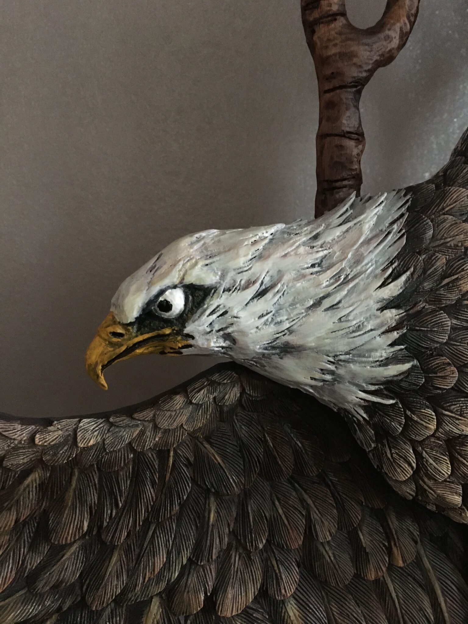 Extreme close-up view of the hand-painted white feathered head, sharp beak, and detailed brown wings of a carved mahogany bald eagle on a custom front door.