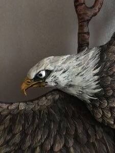 Extreme close-up view of the hand-painted white feathered head, sharp beak, and detailed brown wings of a carved mahogany bald eagle on a custom front door.