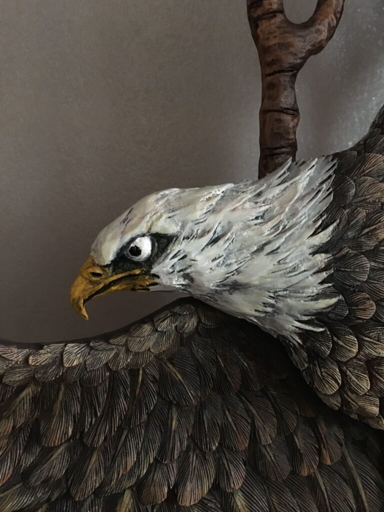 Extreme close-up view of the hand-painted white feathered head, sharp beak, and detailed brown wings of a carved mahogany bald eagle on a custom front door.