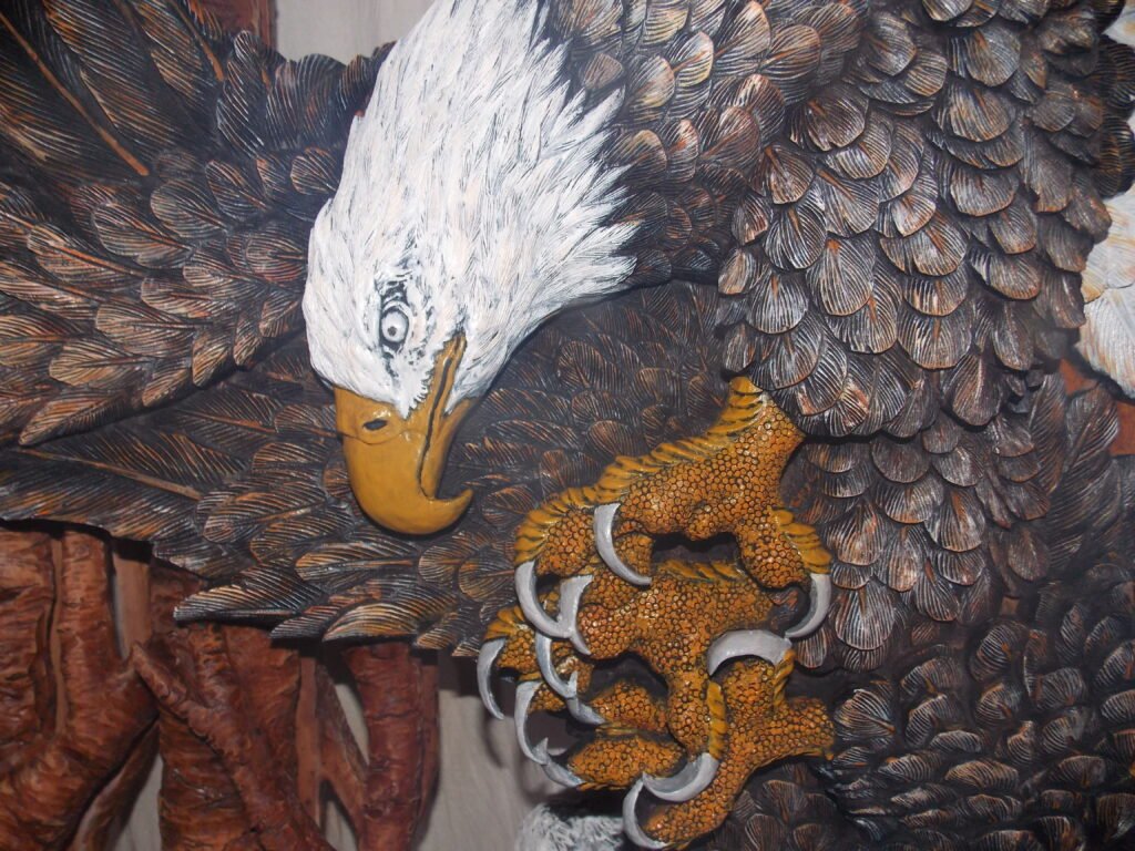 Extreme close-up of a hand-painted solid wood door carving highlighting the detailed head, fierce yellow beak, and sharp claws of a bald eagle.