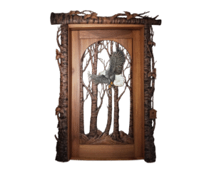 Handcrafted wooden door featuring a detailed carved bald eagle in flight through a forest of trees, framed with rustic log-style bark and leaf accents, custom made by Crown Custom Doors