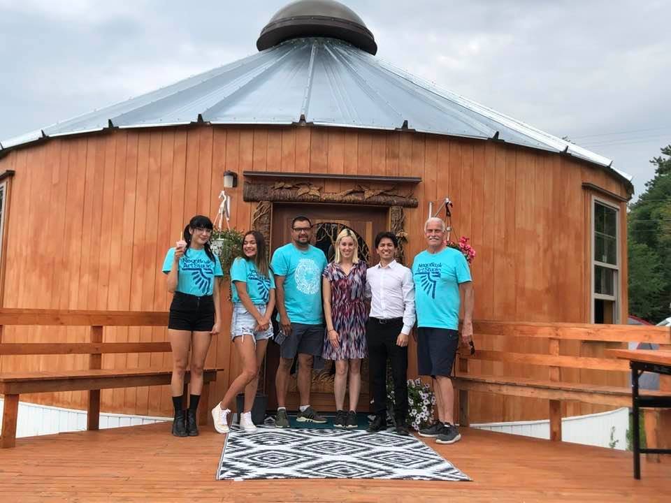 Happy clients standing together on a spacious wooden deck in front of their custom hand-carved solid mahogany bald eagle door installed on a luxury wooden yurt.