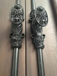 Close-up of a pair of heavy-duty black cremone bolt locks with detailed hand-crafted lion head handles, installed on a rich dark solid wood door.