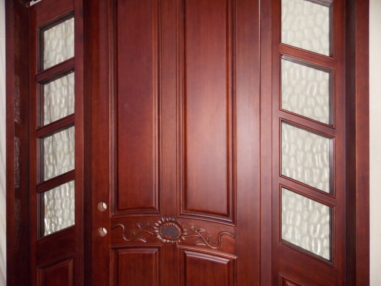 A medium close-up of a custom solid mahogany wood front door showcasing a hand-carved sunflower design and flanked by multi-pane textured water cubic glass sidelights.