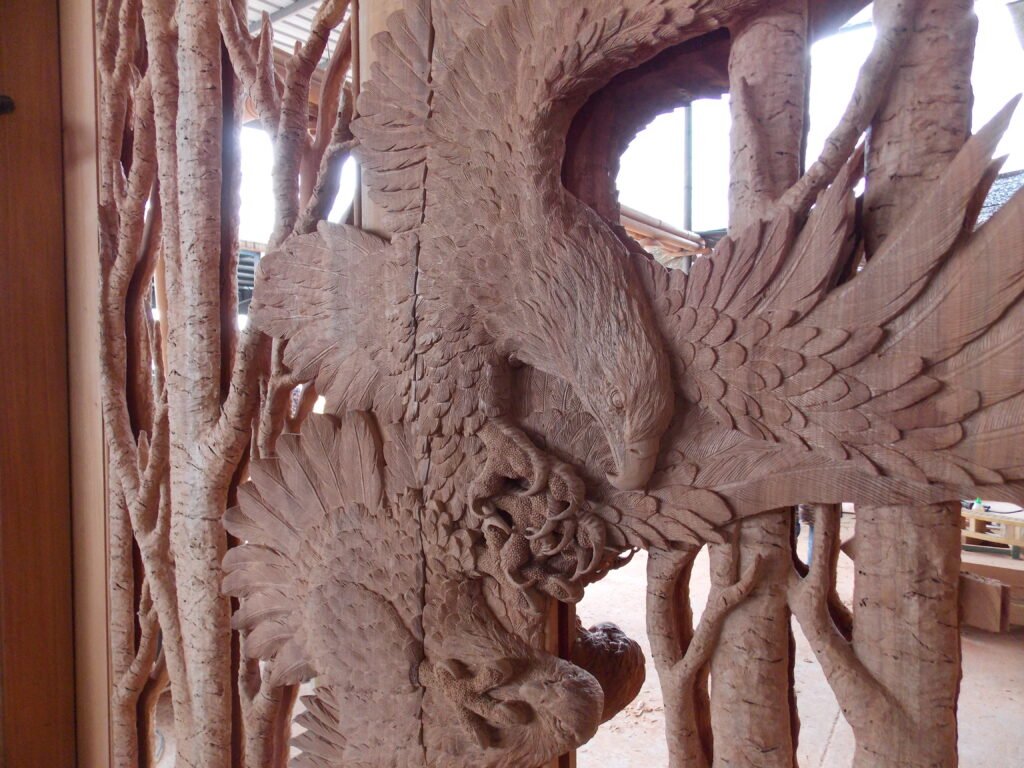Close-up view of an unfinished solid wood door panel featuring two hand-carved eagles in flight surrounded by intricate tree branch openwork.