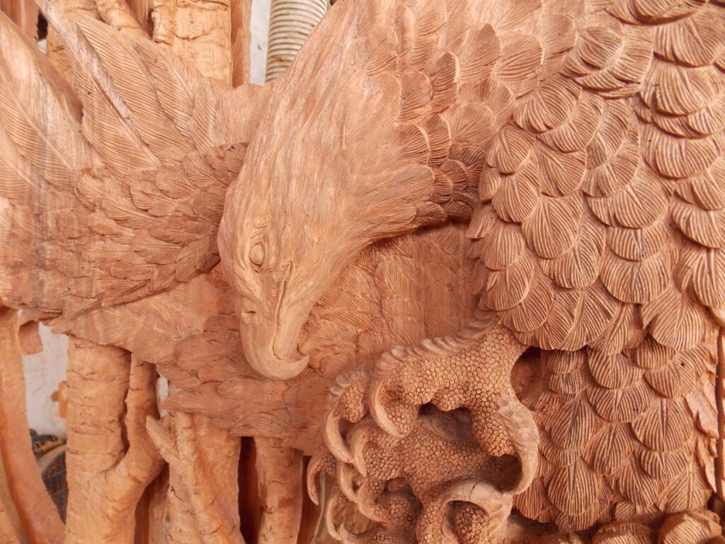 Extreme close-up of raw, unfinished solid wood door panel showing hand-carved eagle feathers, head, and sharp talons in deep relief.