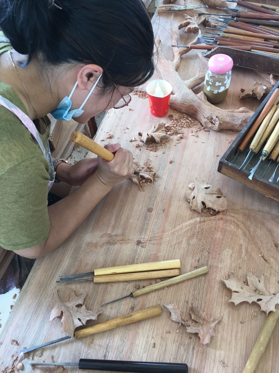 Master woodcarver using traditional hand chisels to carve intricate oak leaf details into solid timber on a workshop workbench surrounded by hand tools at Crown Custom Doors.