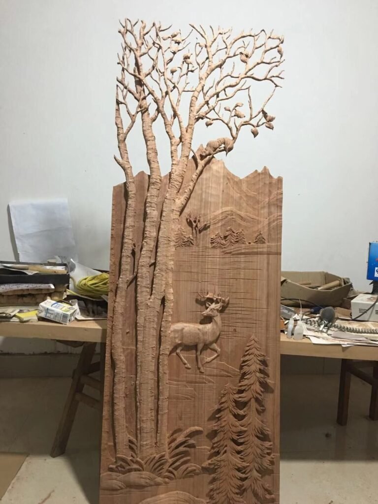 Completed high-relief hand-carved solid wood panel for a custom entry door featuring tall aspen trees with squirrels, a realistic deer by a mountain lake, pine trees, rocks and distant peaks; shown upright in the Crown Custom Doors workshop