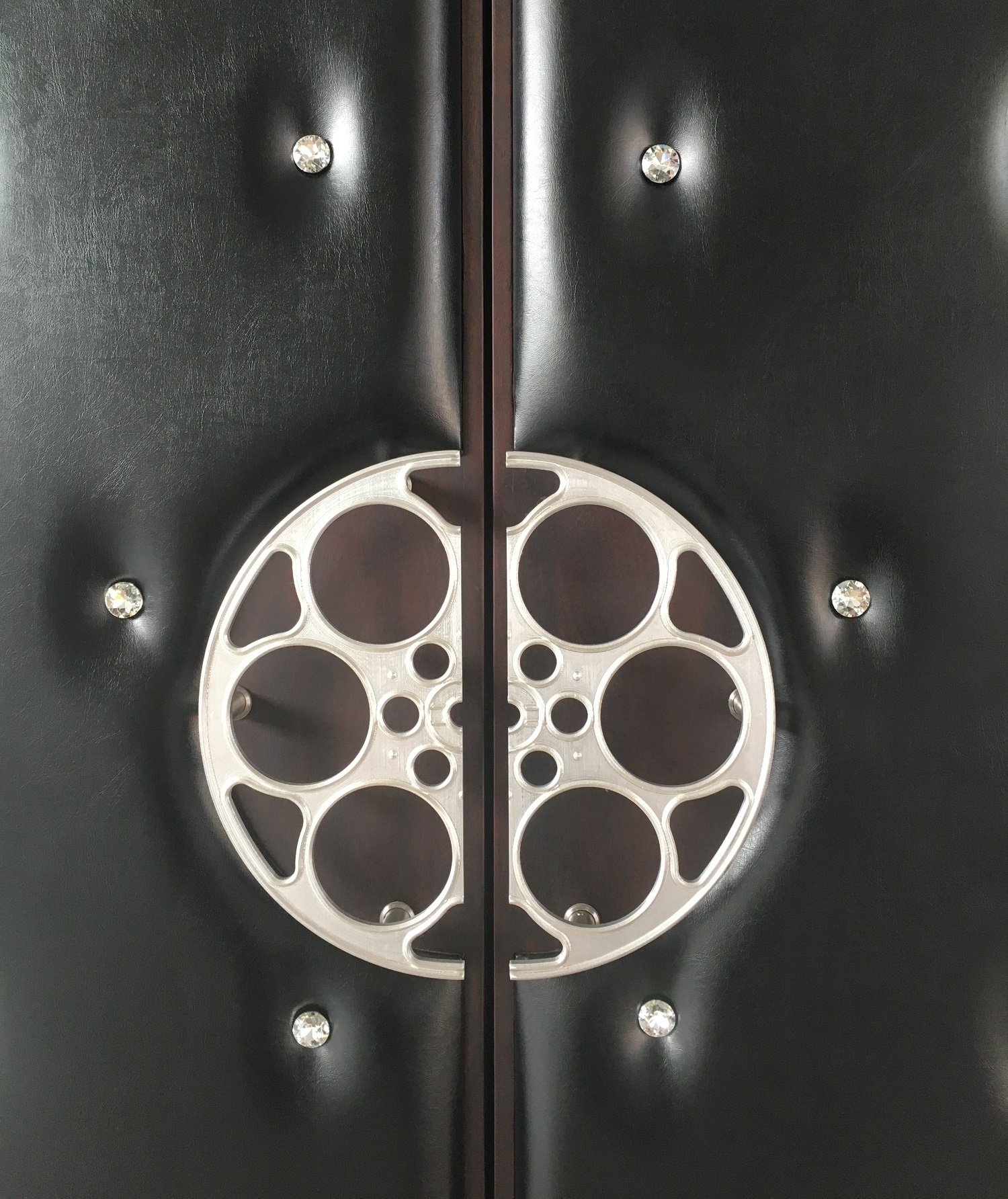 Close-up of luxury black tufted leather acoustic home theater double doors featuring crystal stud accents and custom silver film reel pull handles.