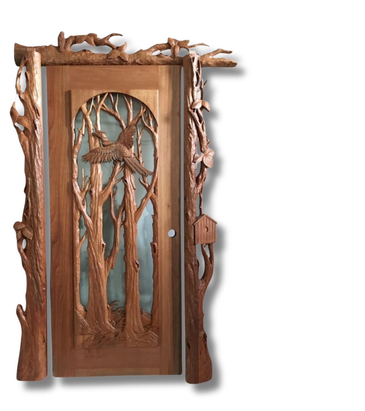 Craftsman solid wood entry door featuring an arched glass panel with a 3D relief carving of a flying bird amidst trees, framed by sculptured branch jambs and a carved birdhouse detail.