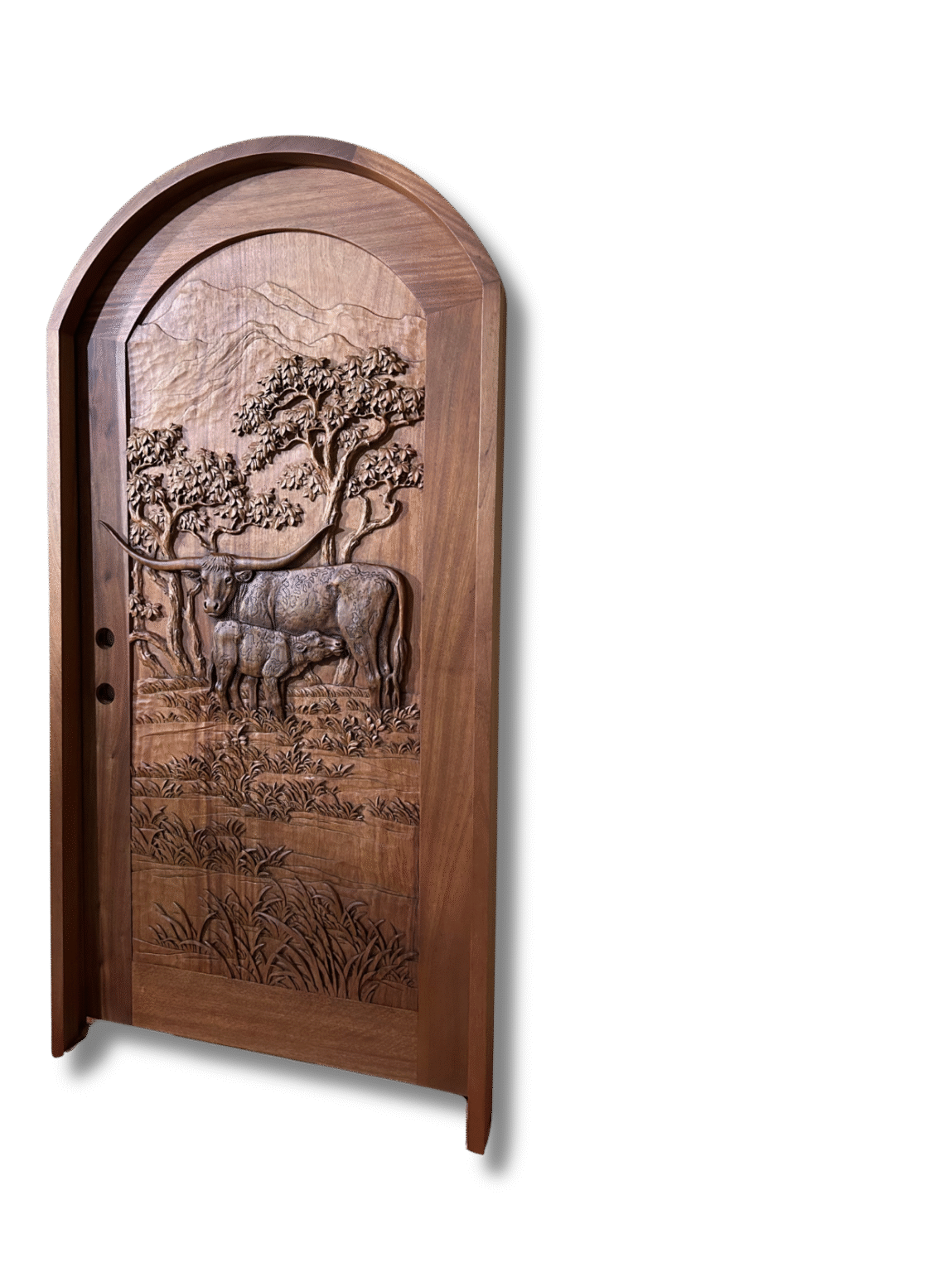 Arched solid wood entry door featuring a detailed 3D relief carving of a Texas Longhorn cow nursing a calf in a Western ranch landscape with trees and mountain backdrop.
