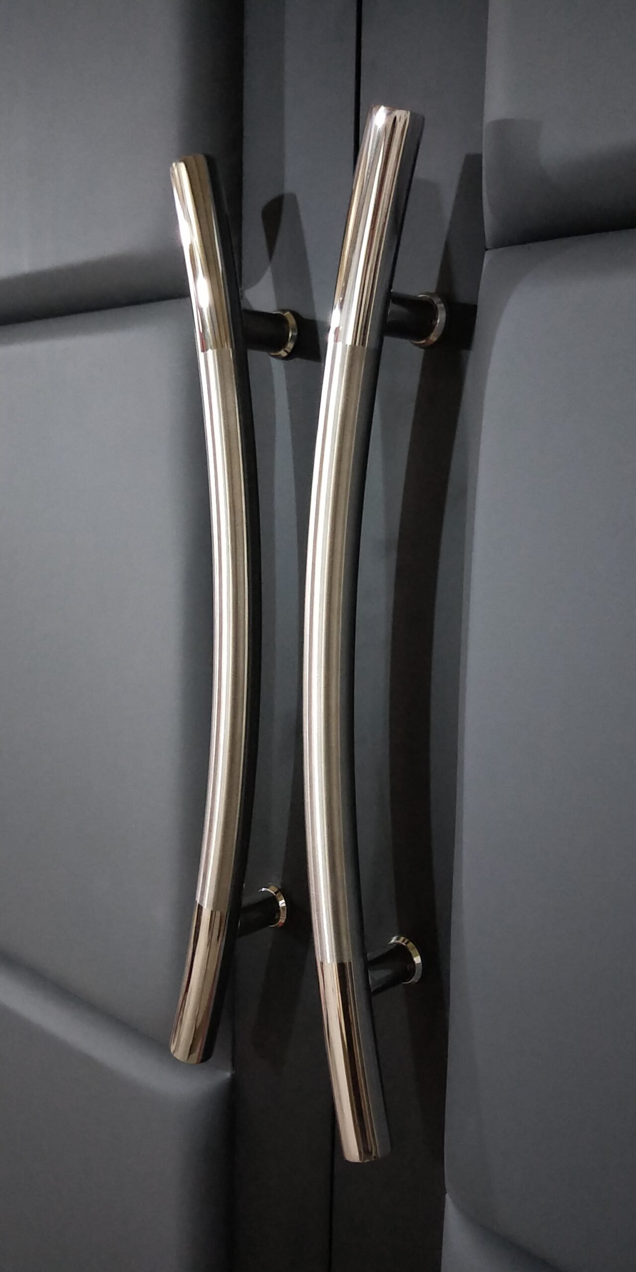 Extreme close-up of sleek 24-inch polished chrome curved ladder handles mounted on Storm Gray vinyl padded acoustic panels of the Gibson home theater double doors by Crown Custom Doors.