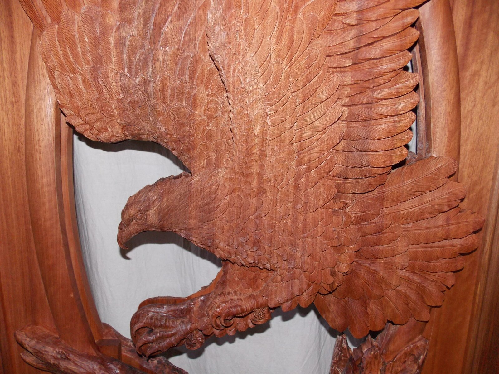 Close-up photo highlighting the intricate hand-carved feather textures, sharp talons, and detailed beak of a bald eagle wood carving on a solid mahogany entry door panel.