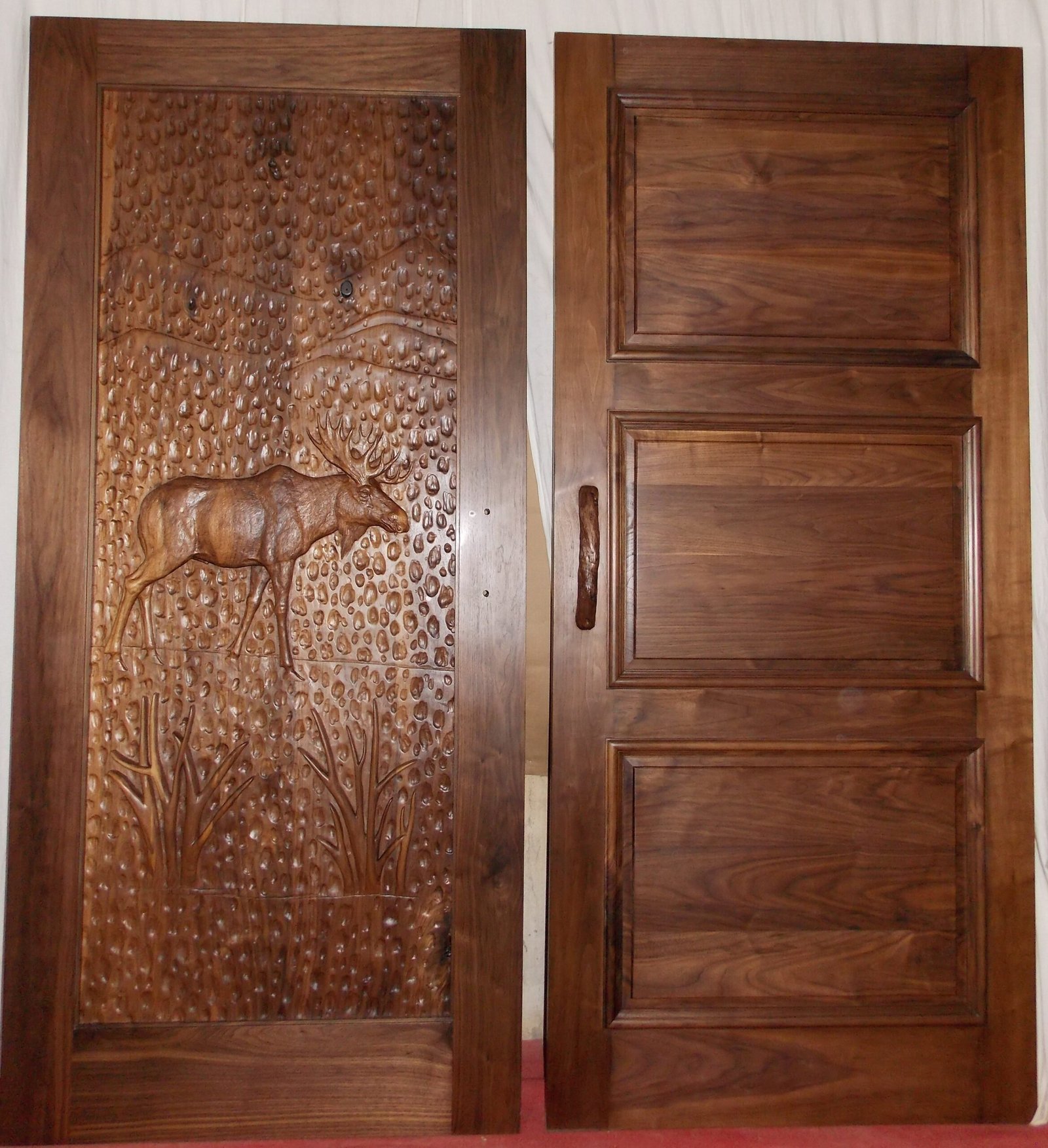 Full-length side-by-side view showing the front carved panel featuring a bull moose and the back 3-panel interior layout of a solid black walnut door for a mountain lodge.