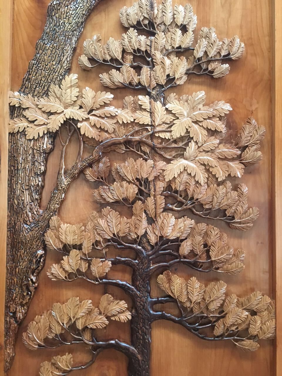 Detailed close-up of a 3D hand-carved solid wood panel featuring textured bark and layered oak and pine foliage for a custom architectural entry door.