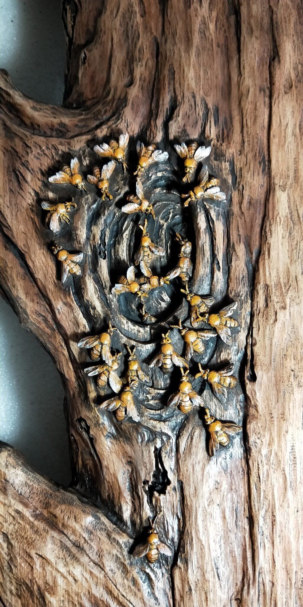 Close-up shot of a solid wood door panel featuring high-relief, hand-carved, and hand-painted honeybees clustering around a textured, hollowed-out tree trunk knot with rich dark wood grain.