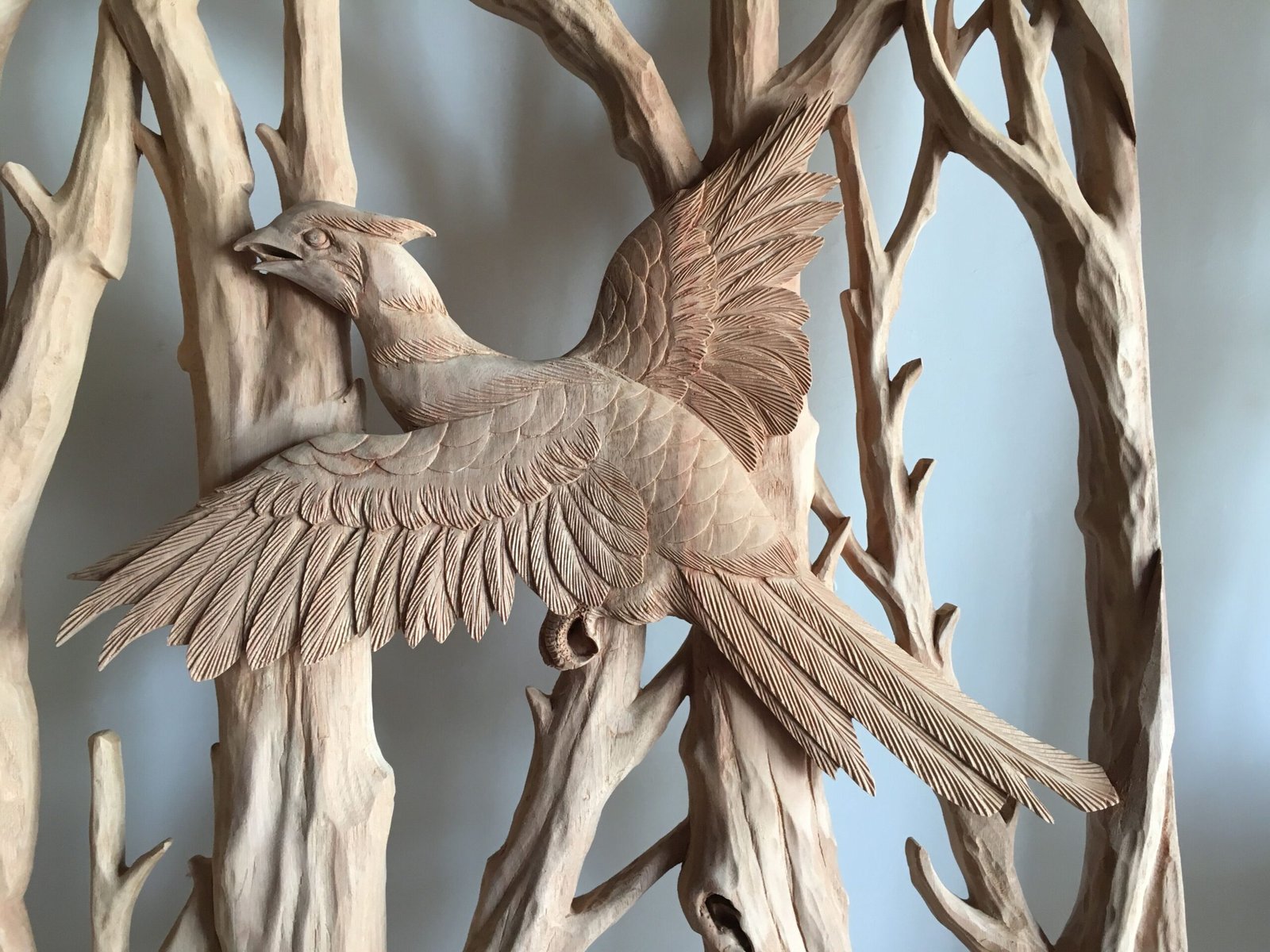 Close-up of an unfinished solid wood panel showing a hand-carved 3D flying pheasant with detailed wing feathers, talons, and forest tree branches by Crown Custom Doors.