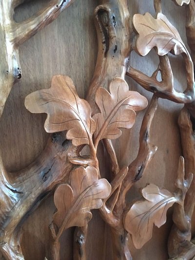 Crown Custom Doors high-relief close-up showing hand-carved solid wood oak leaves, veins, and organic tree branch textures on a custom architectural door.