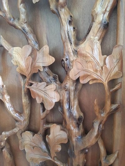 Crown Custom Doors macro close-up view showing deep relief hand-carved solid wood oak leaves and natural tree branch textures on a custom door.
