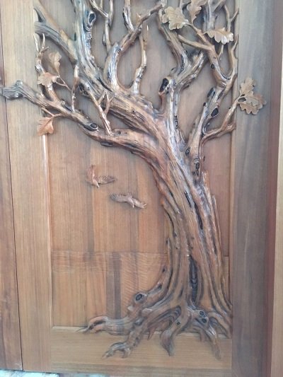 Crown Custom Doors full panel view featuring a hand-carved solid wood gnarled oak tree trunk with spreading branches, oak leaves, and two flying birds.