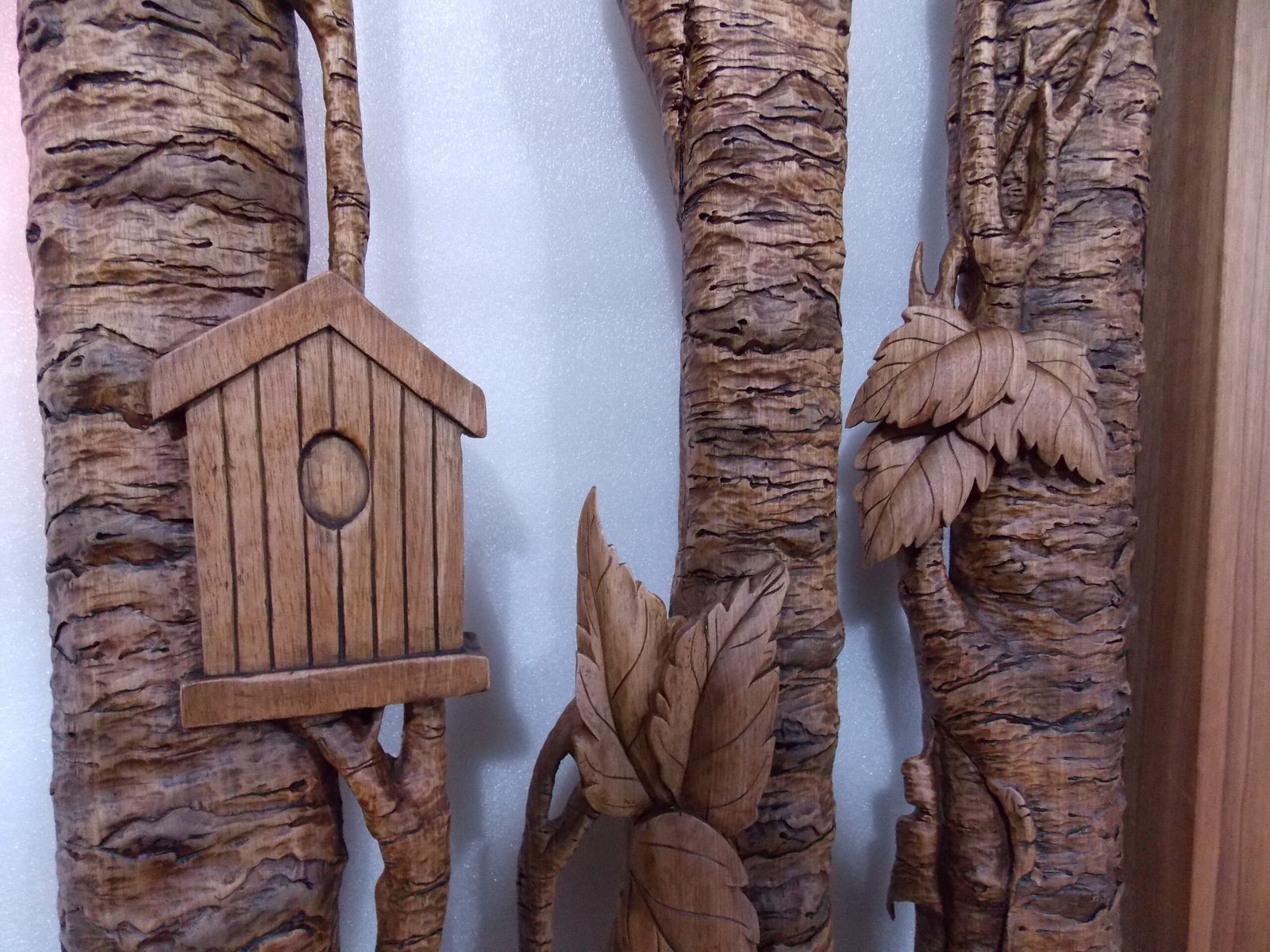 Extreme close-up view of 3D hand-carved solid wood door casings sculpted to resemble realistic tree bark, featuring detailed leaves and a miniature carved wooden birdhouse.